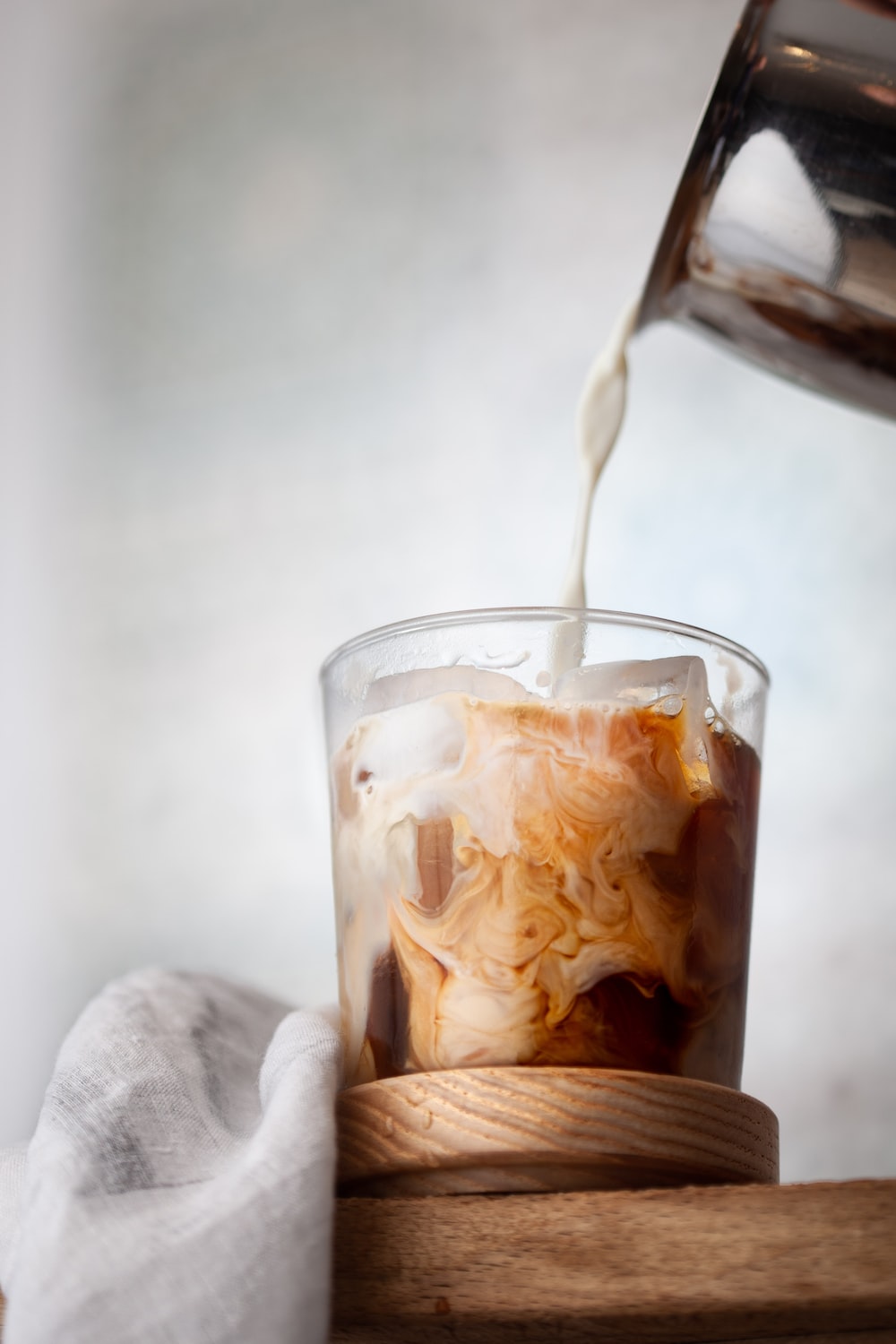 A glass of iced coffee with milk being poured into it. - Coffee