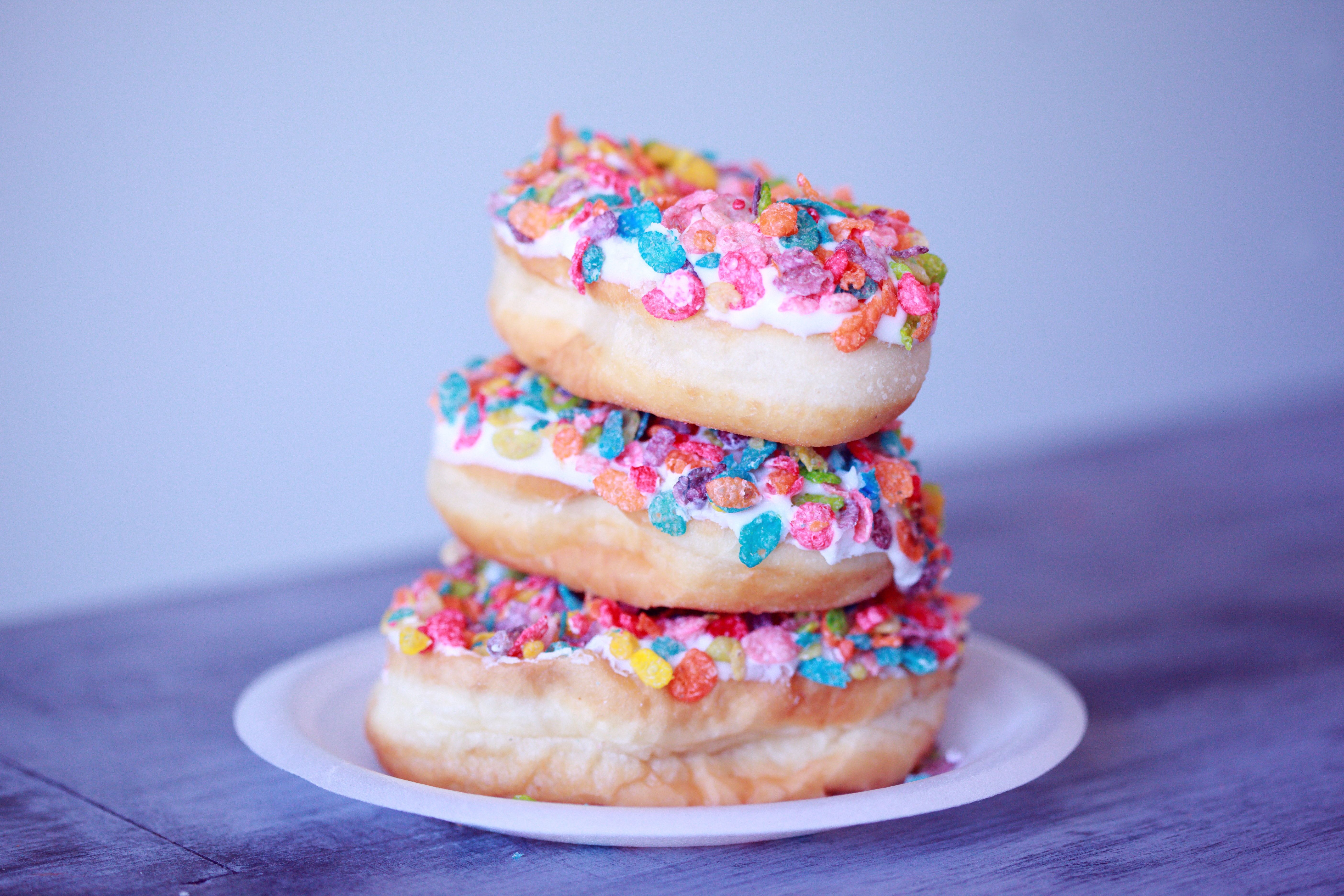 A stack of three fruity pebbles covered donuts on a white plate. - Food