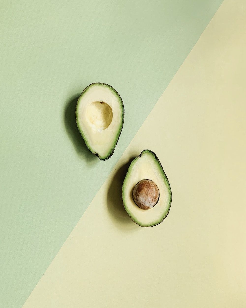 An avocado cut in half on a green and yellow background - Avocado