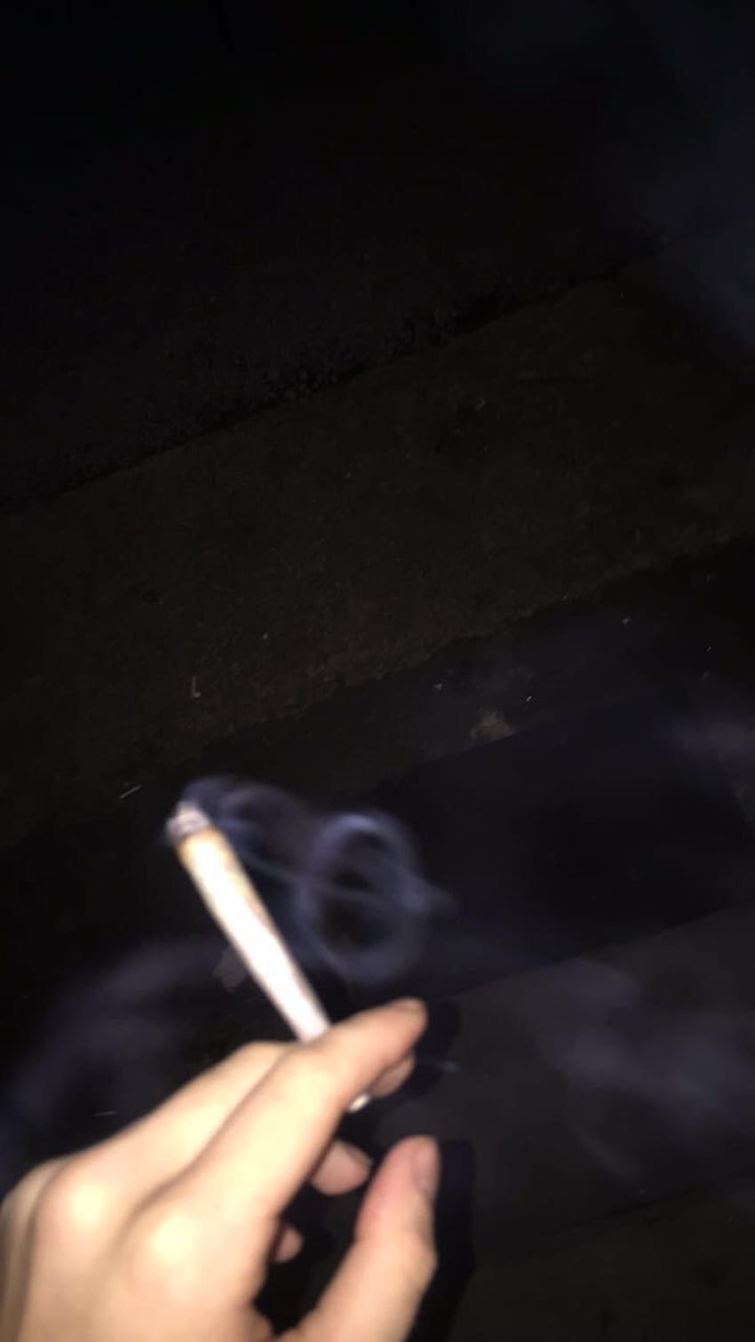 A person holding up their cigarette in the dark - Smoke