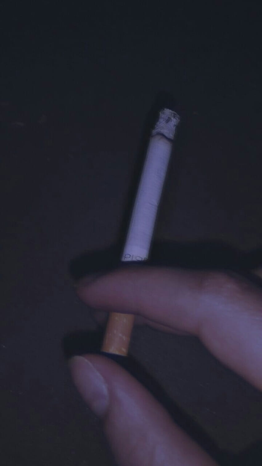 A hand holding a lit cigarette in the dark. - Smoke