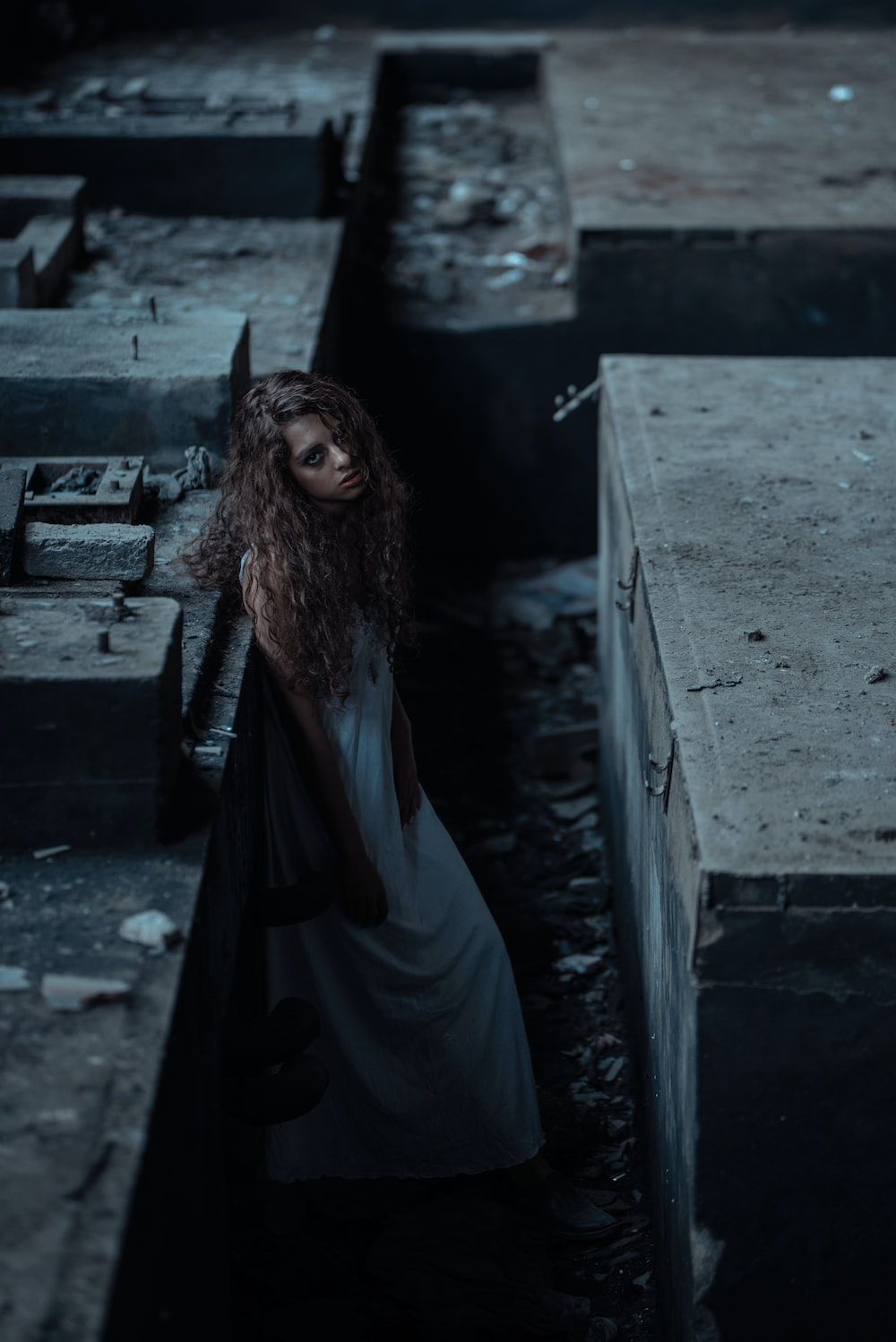 A woman with long hair in a white dress standing in a dark alleyway - Vampire