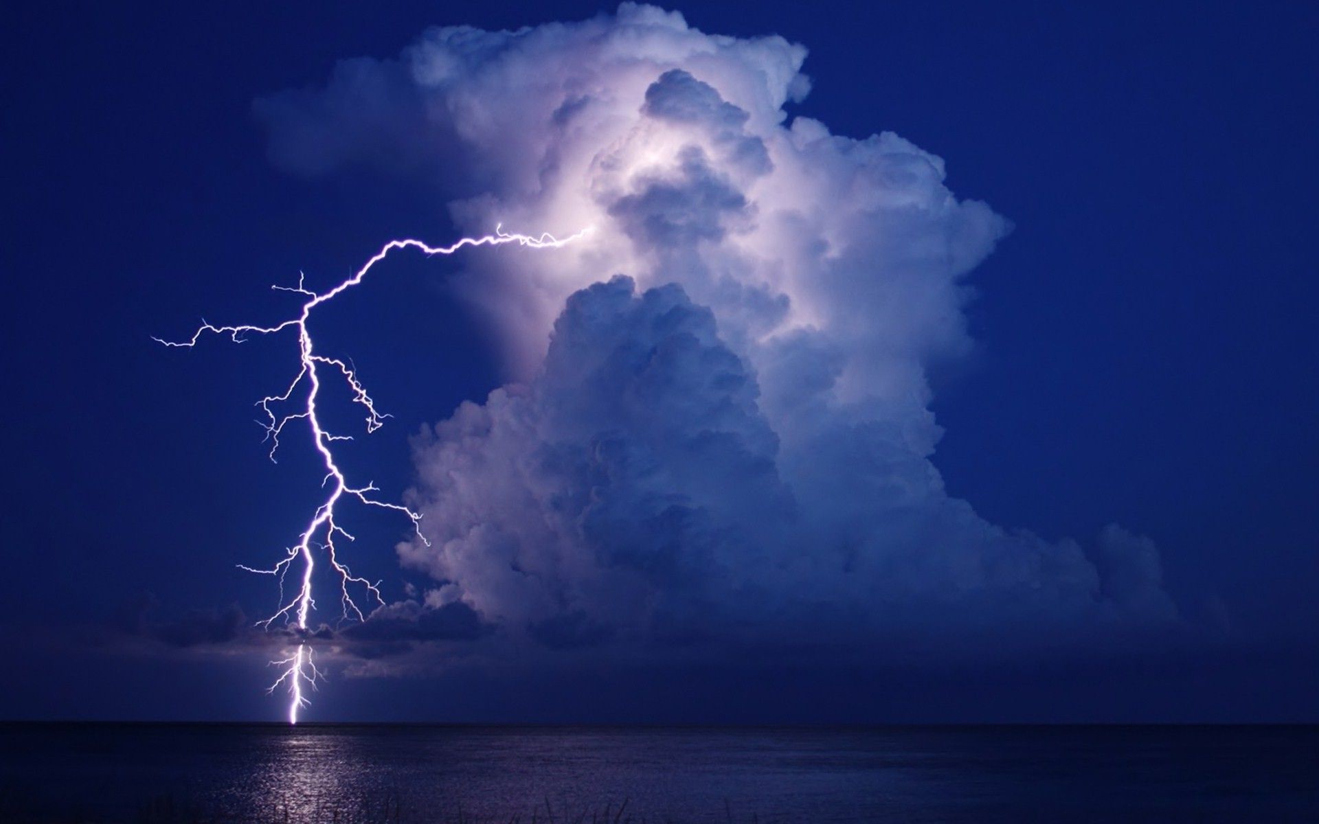 A lightning bolt strikes the ocean in front of a large cloud. - Lightning
