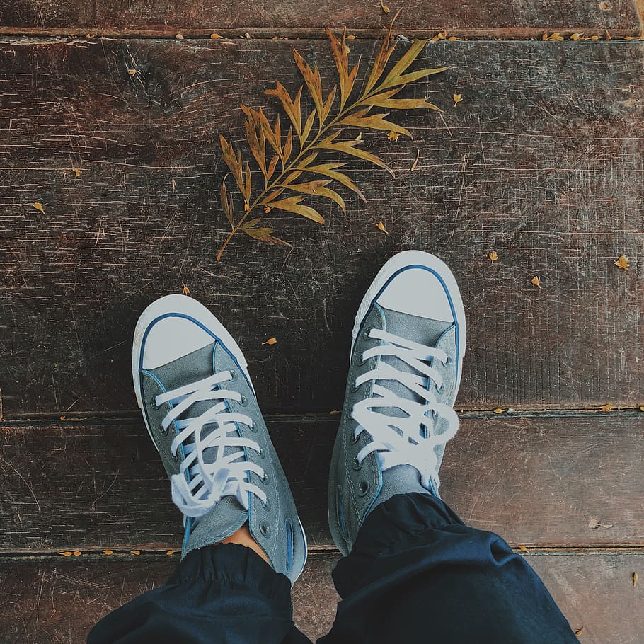 A person wearing blue sneakers standing on a wooden floor - Converse