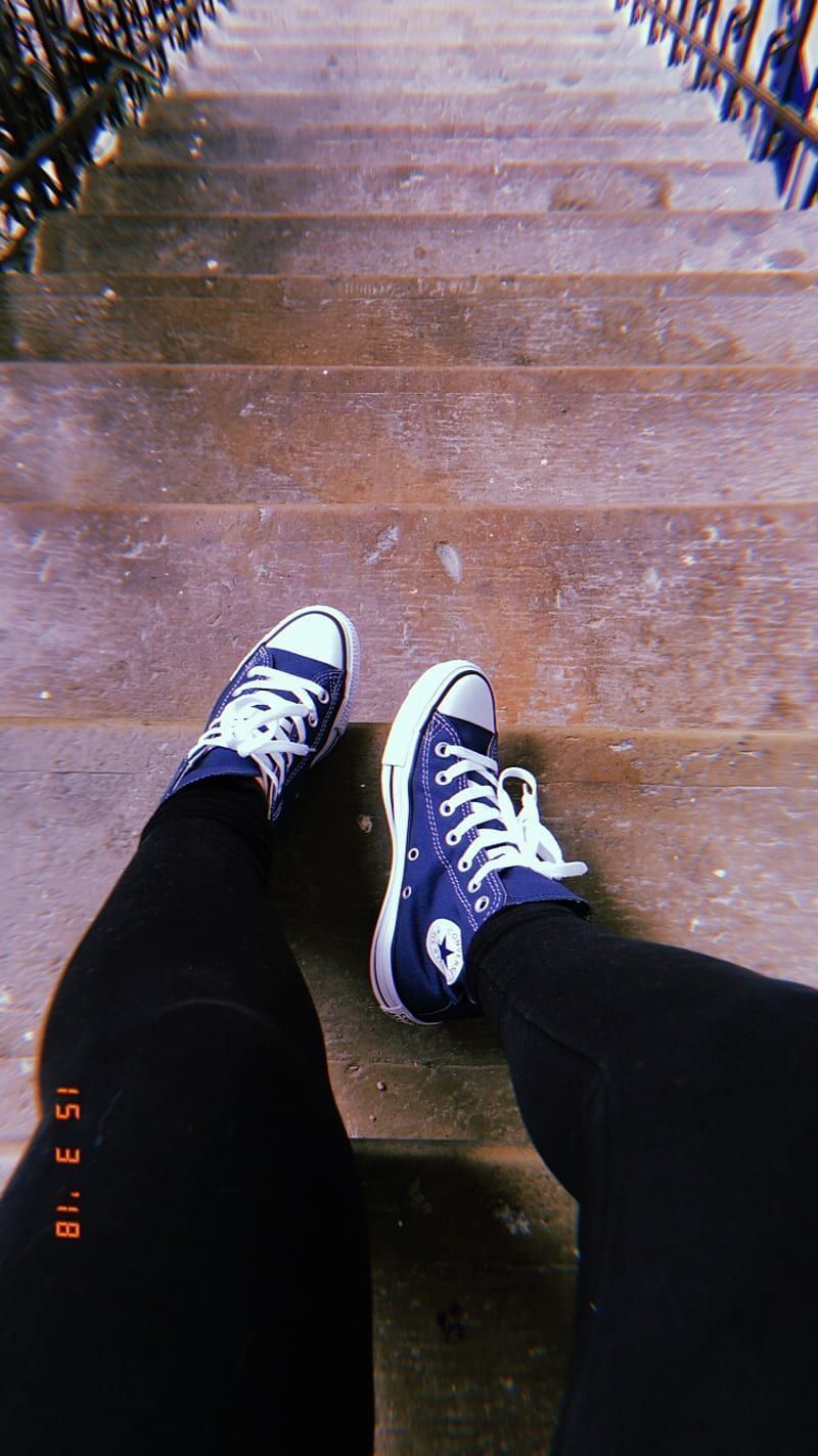 A person is standing on steps with their shoes - Converse