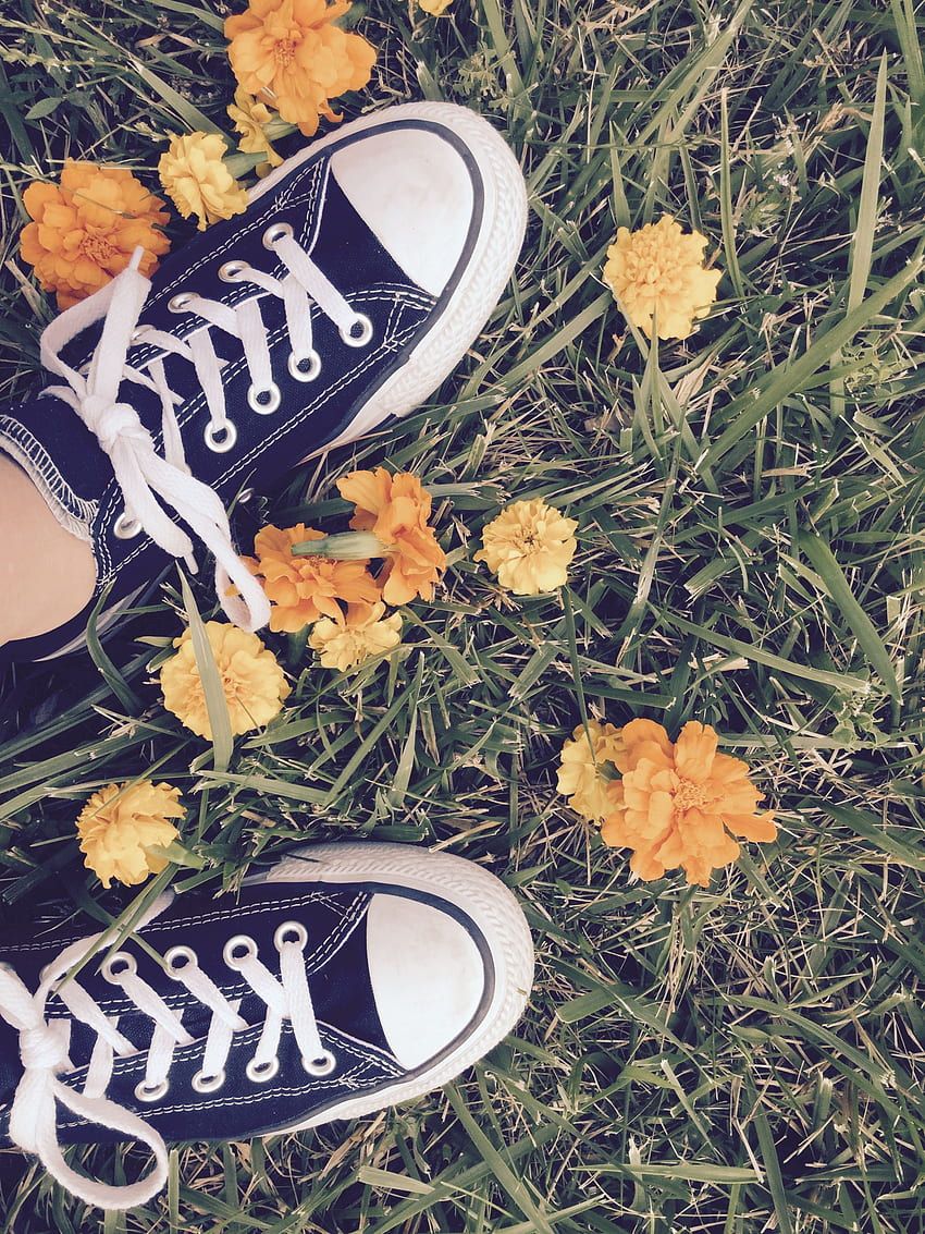 A person's feet are standing on top of some flowers - Converse