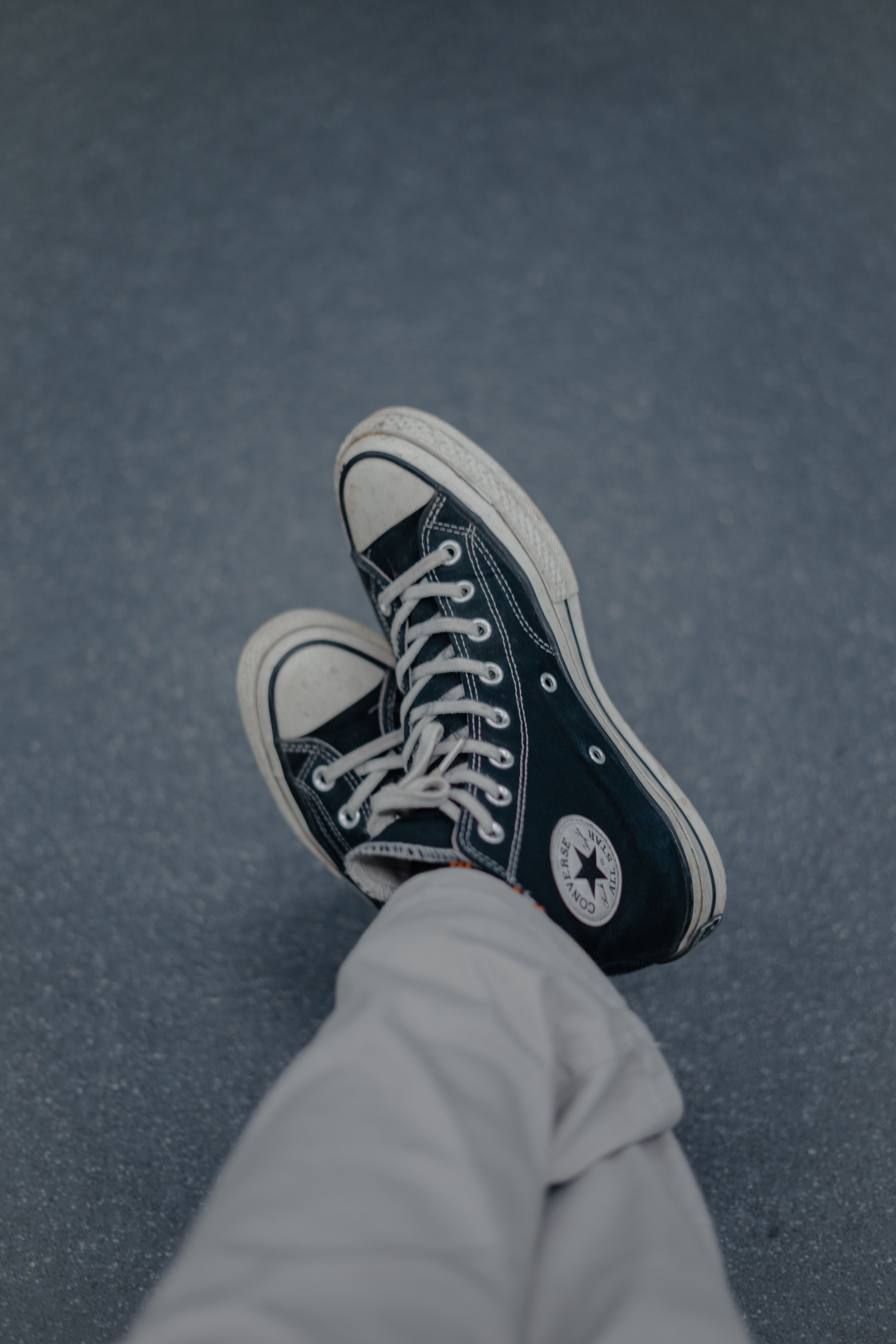 A person is wearing black and white sneakers - Converse