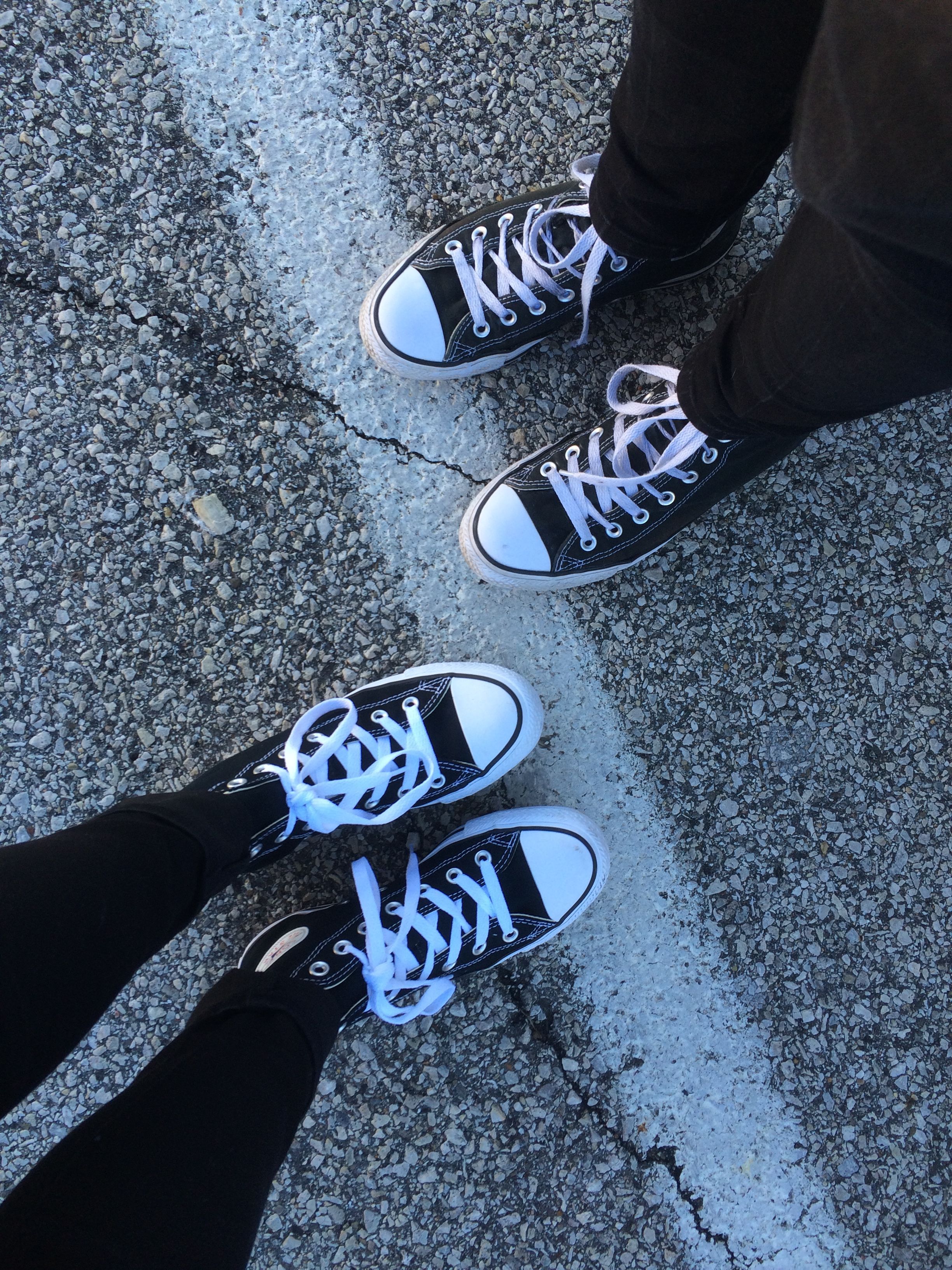 A pair of feet wearing black Converse sneakers. - Converse