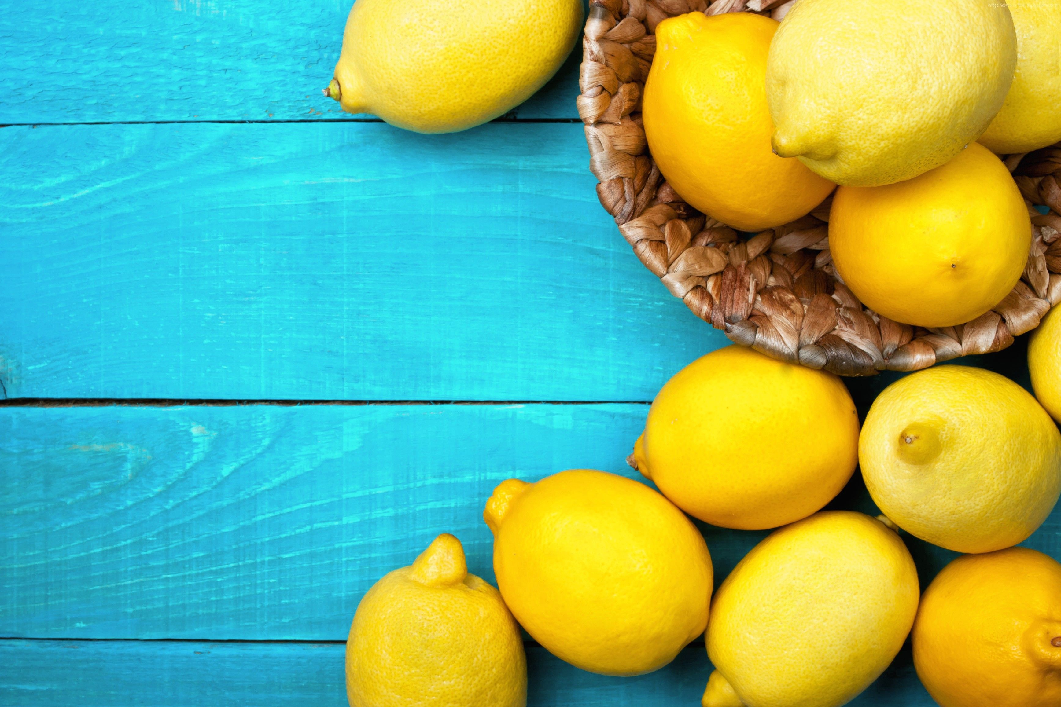 A wicker bowl of lemons on a blue wooden table. - Lemon