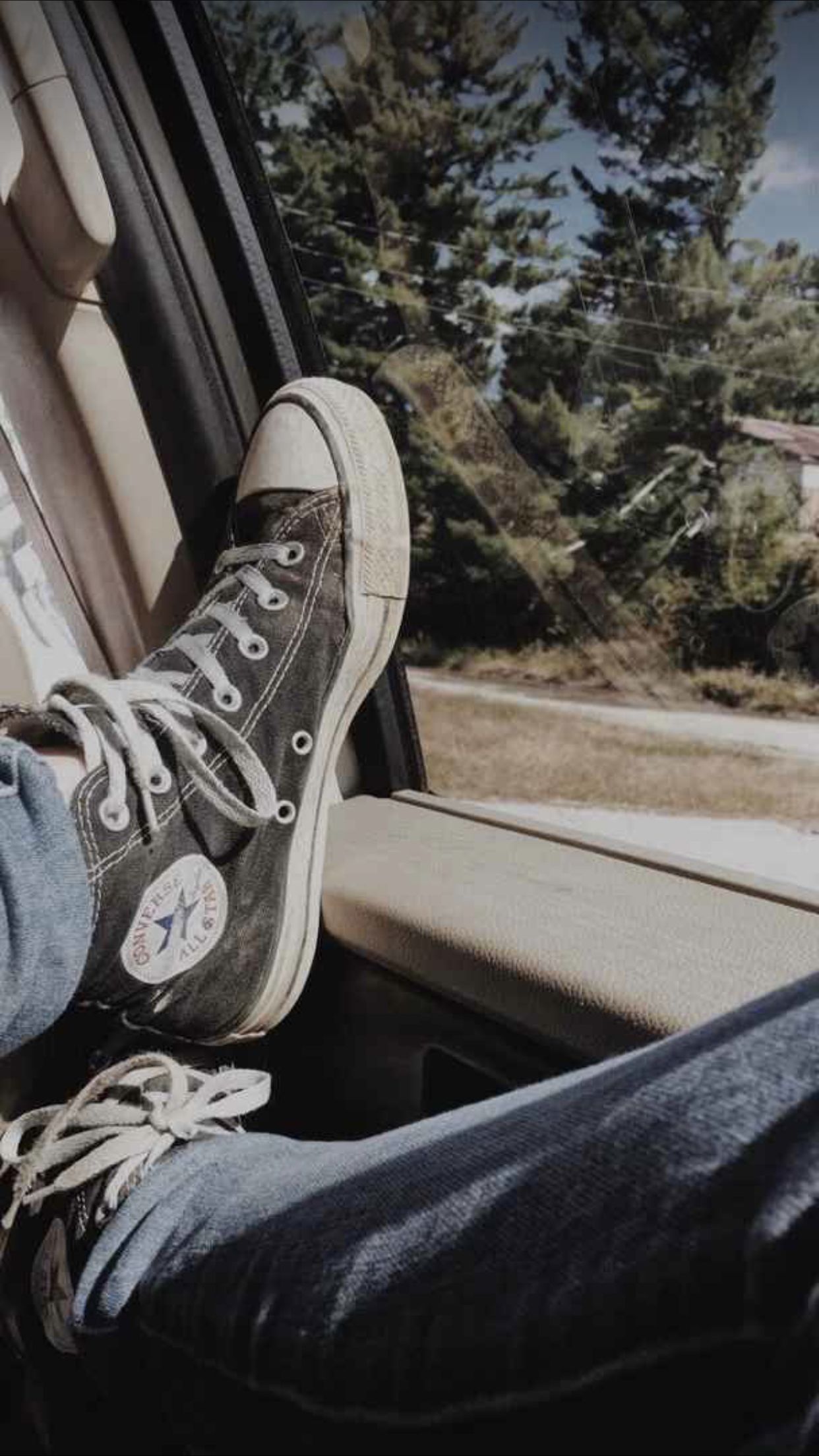 A person's feet are sticking out of a car window. - Converse