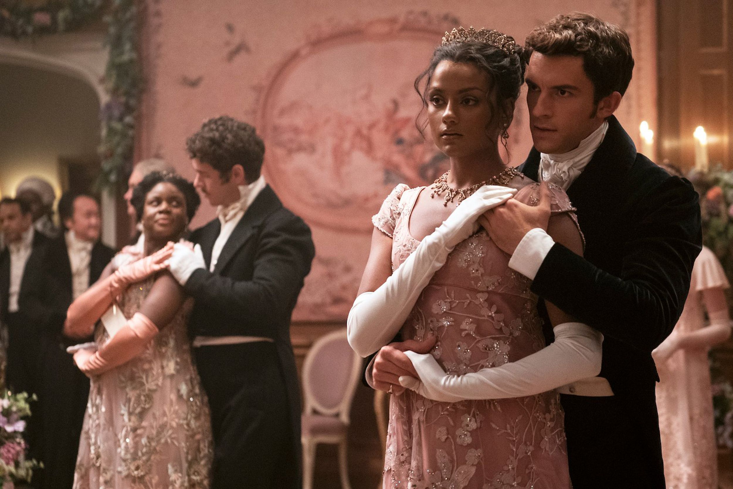 A Black woman in a pink ballgown dances with a white man in a black suit in a scene from Bridgerton. - Bridgerton