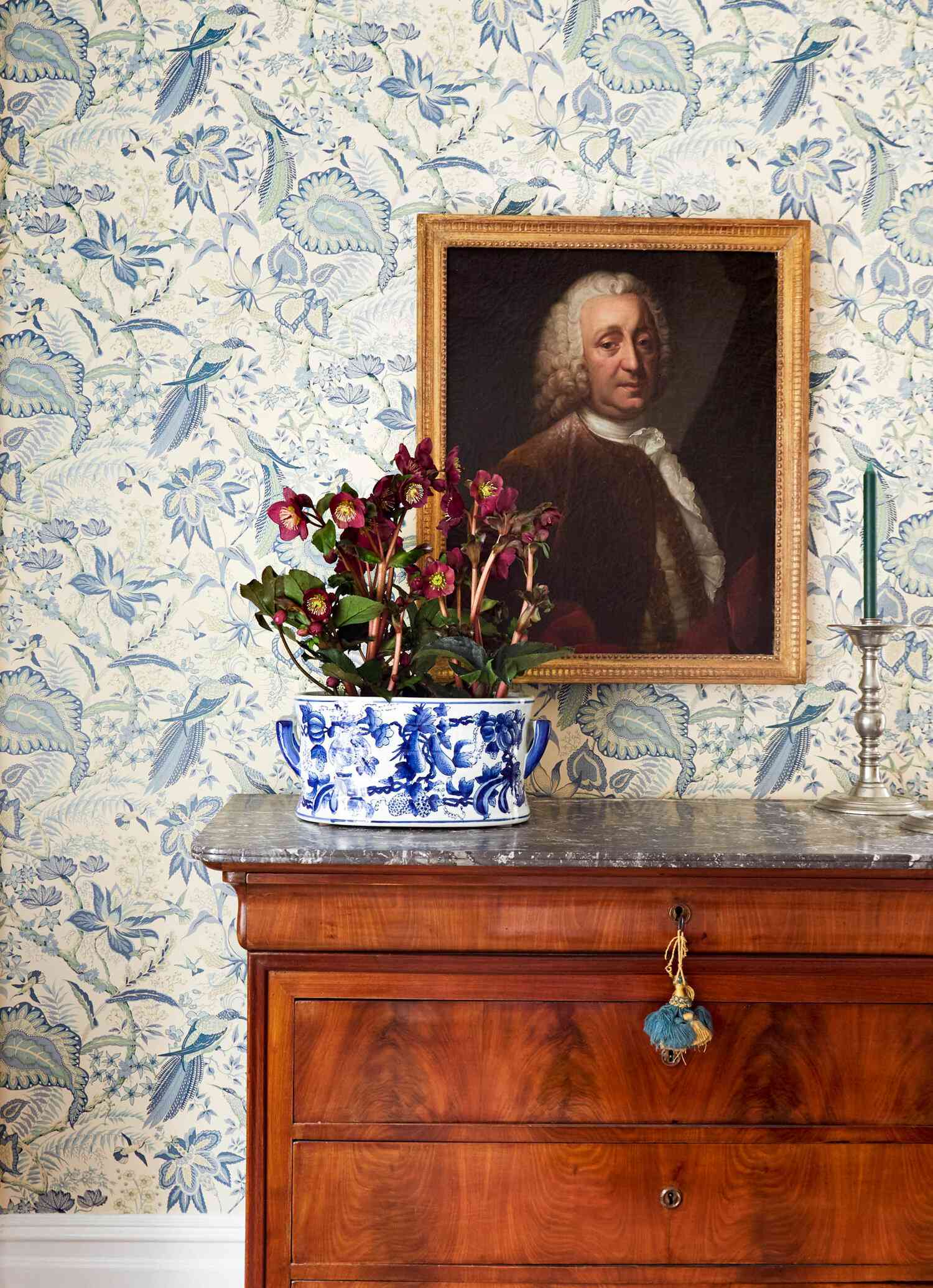 A portrait of the homeowner's great-grandfather hangs above a blue and white antique bowl holding a bouquet of flowers. - Bridgerton