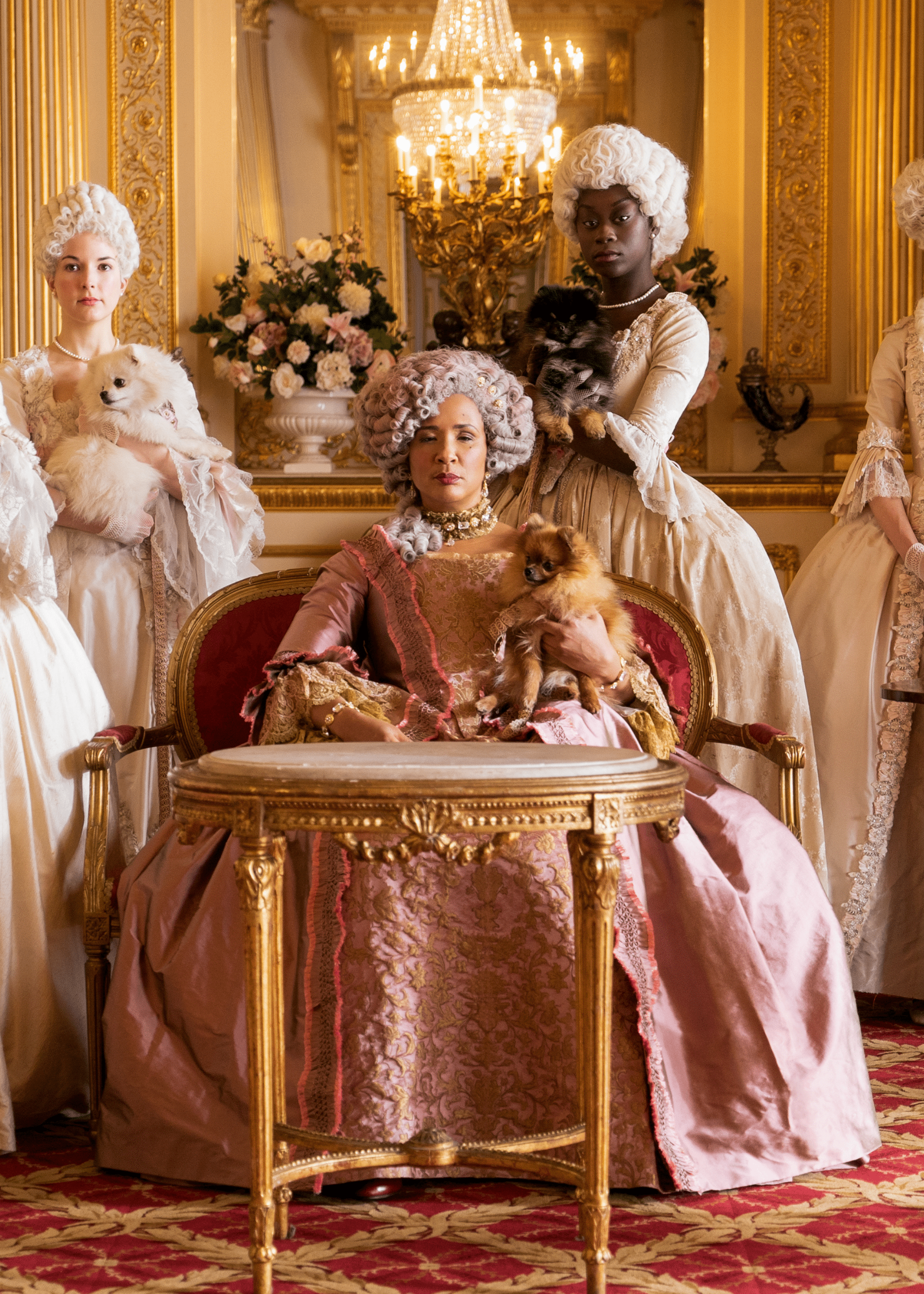 Three women in 18th century baroque gowns, one holding a dog. - Bridgerton