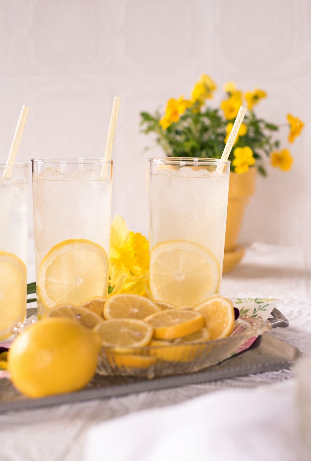 Two glasses of lemonade with yellow flowers in the background. - Lemon