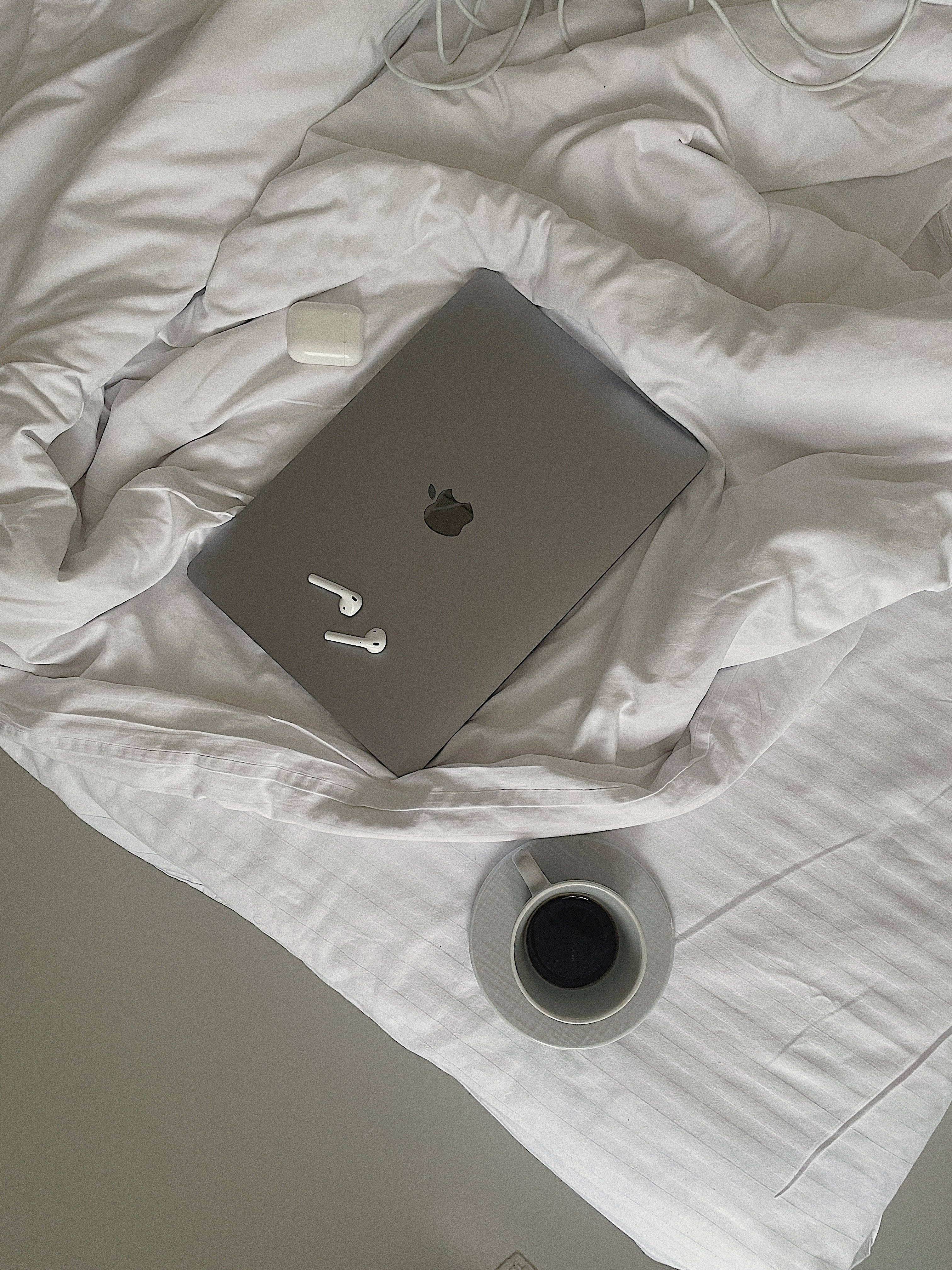 A laptop, earbuds, and a cup of coffee on a bed. - Silver