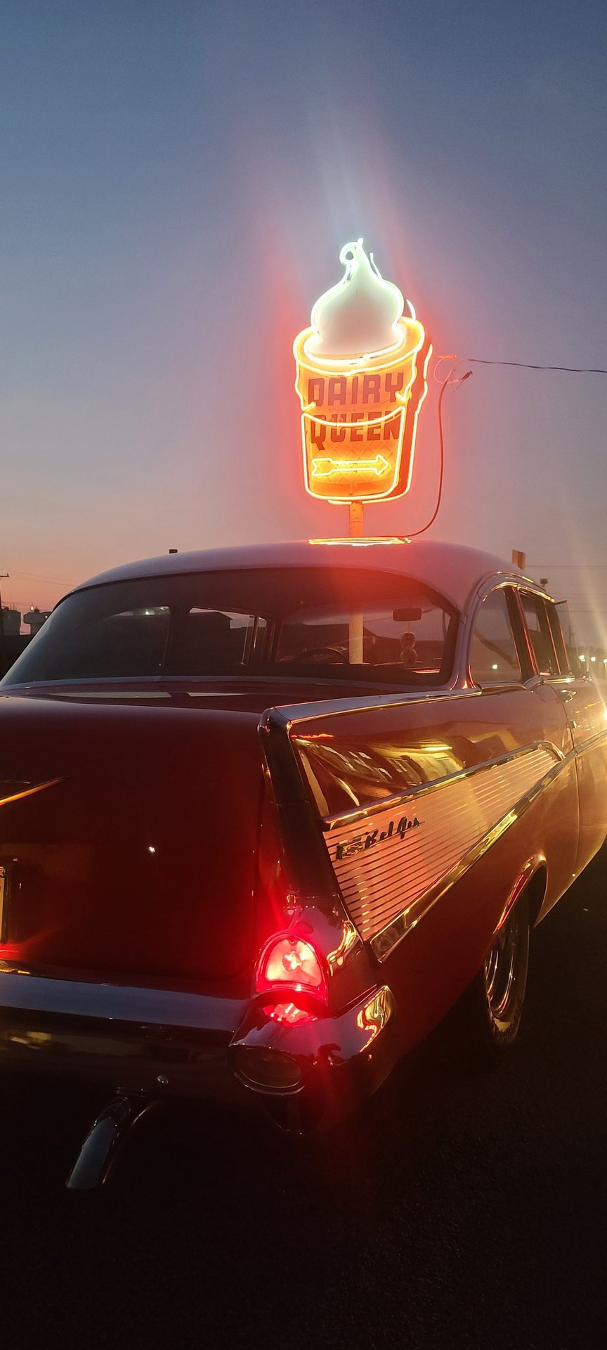 A classic car is parked in front of a neon ice cream sign. - 50s