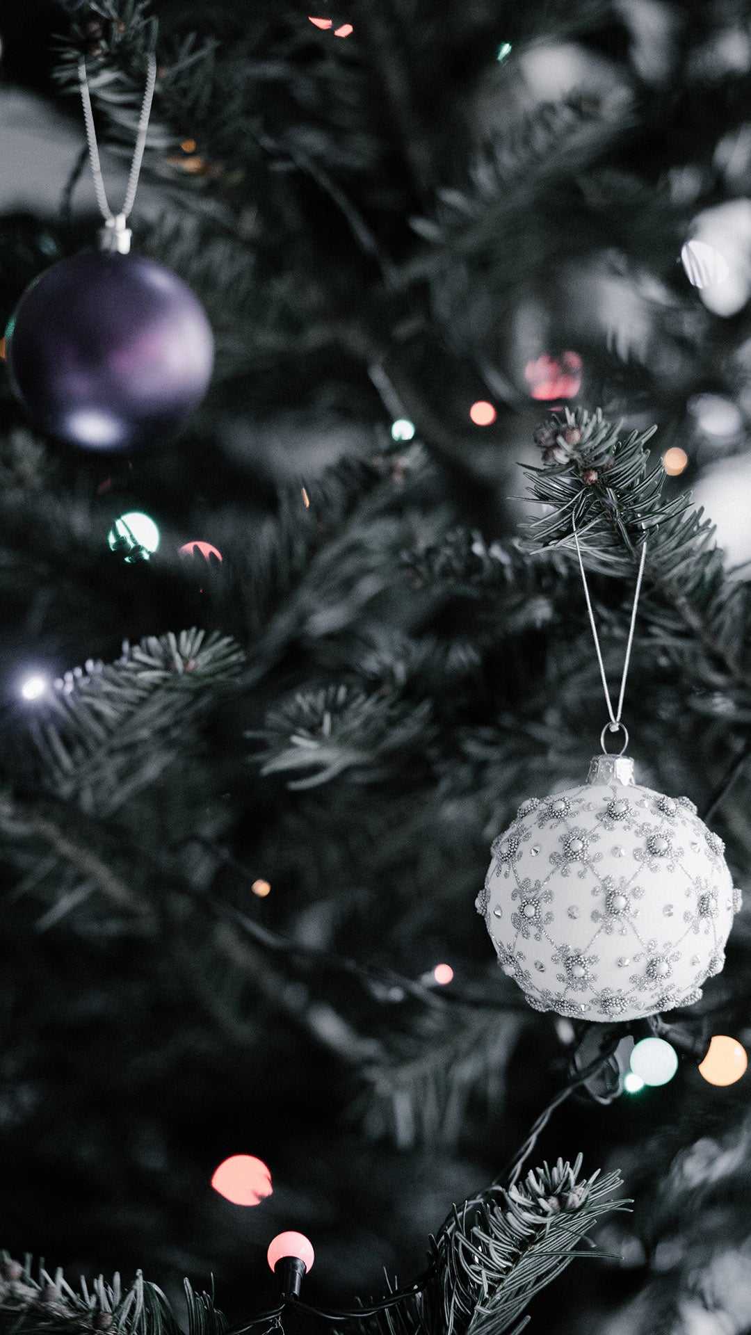 IPhone wallpaper with a close up of a Christmas tree with purple and white ornaments. - Christmas