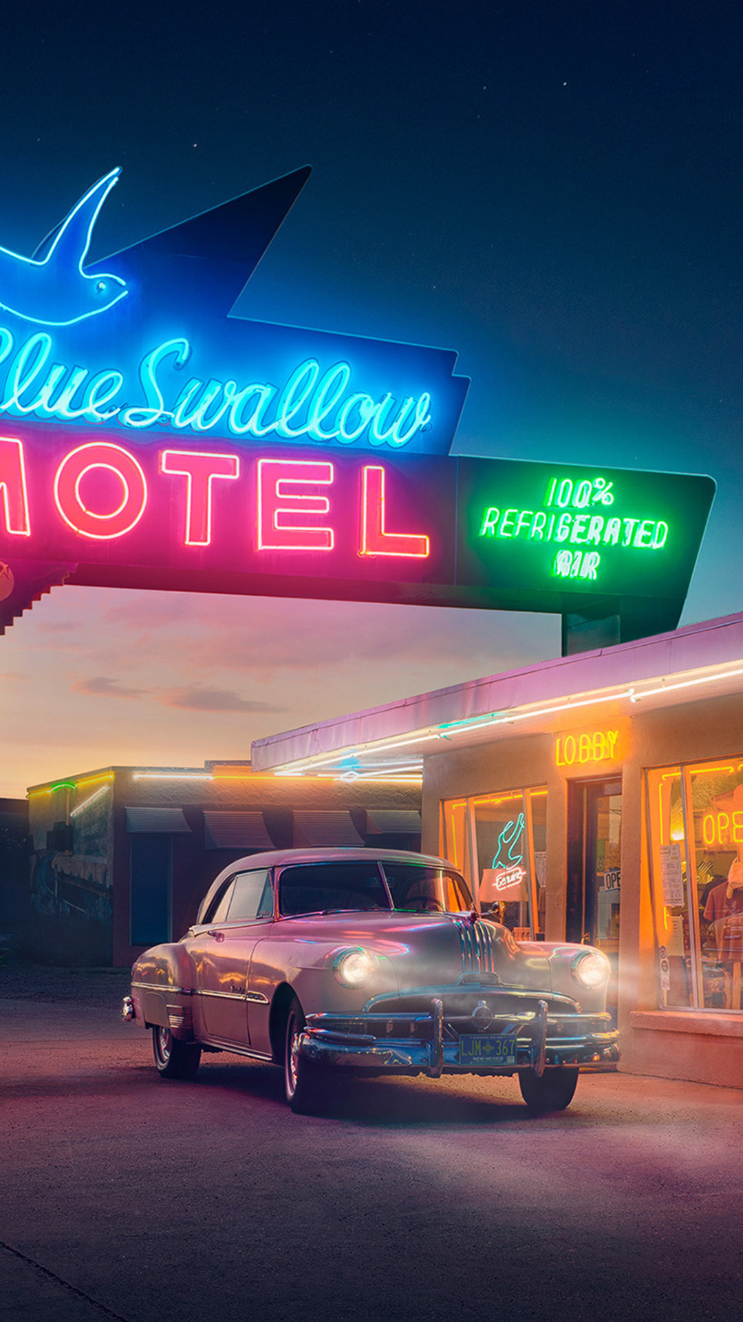 A vintage car parked in front of a neon motel sign at night. - 50s