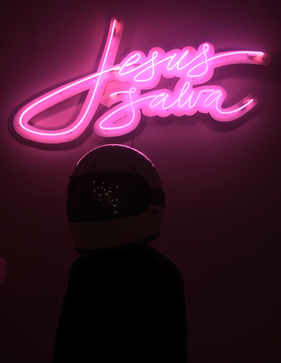 A person wearing a helmet standing under a neon sign that says 