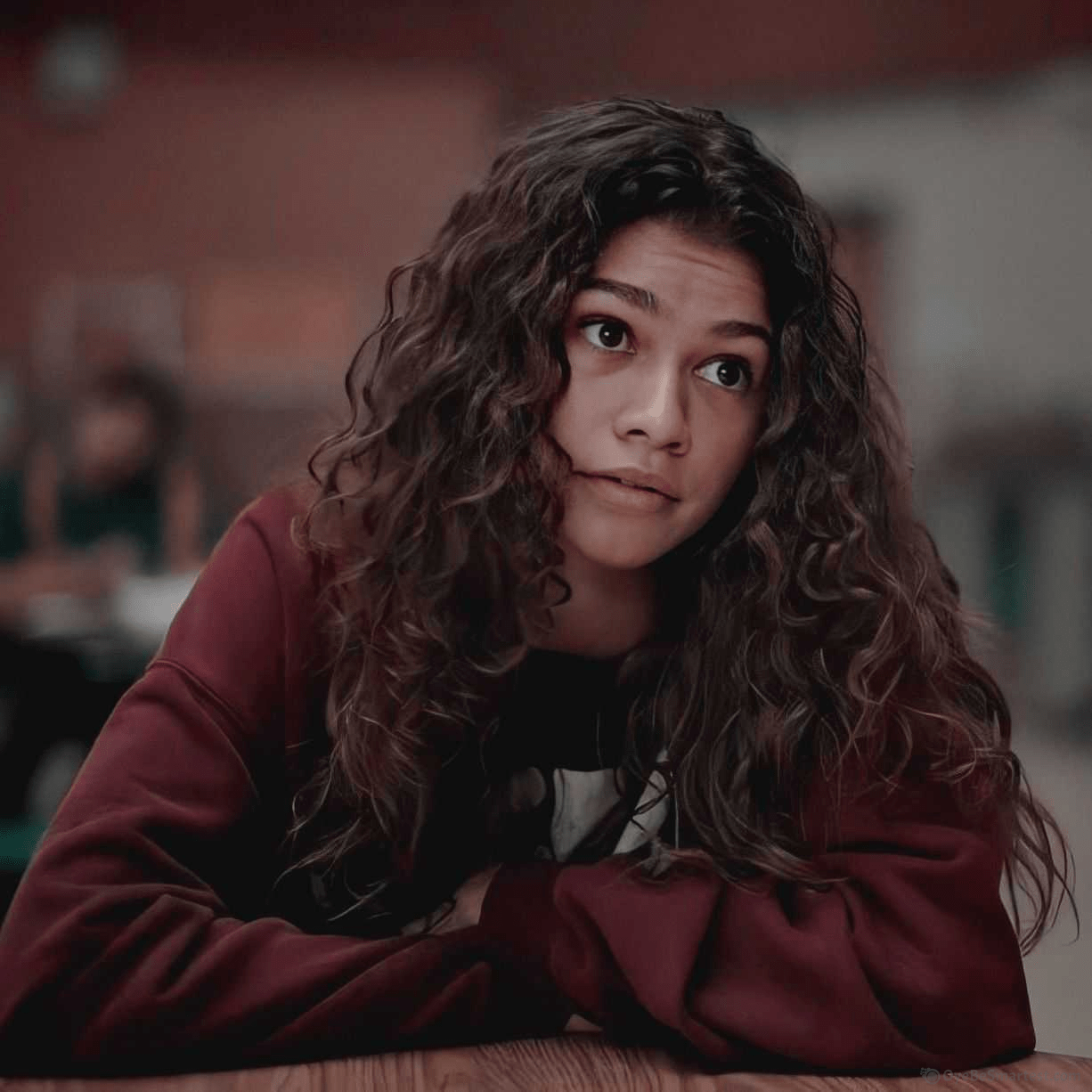 A woman with curly hair sitting at a table. - Euphoria, Zendaya