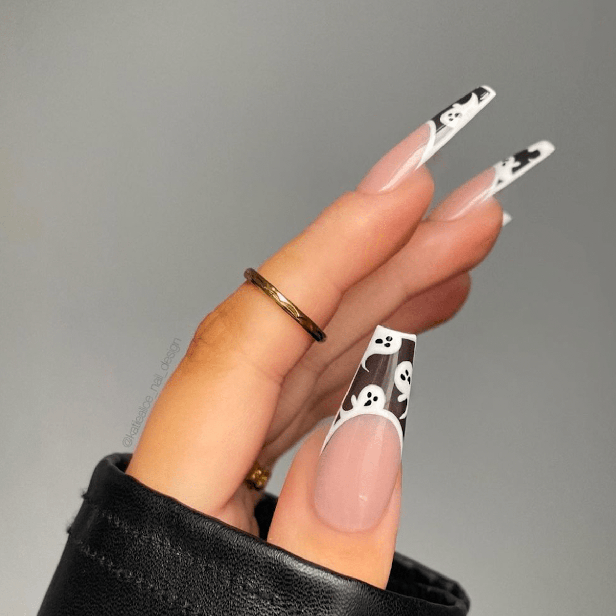 A woman's hand with long, false nails decorated with a black and white ghost pattern. The nails are painted a natural beige tone and the ghosts are painted in black and white. - Nails