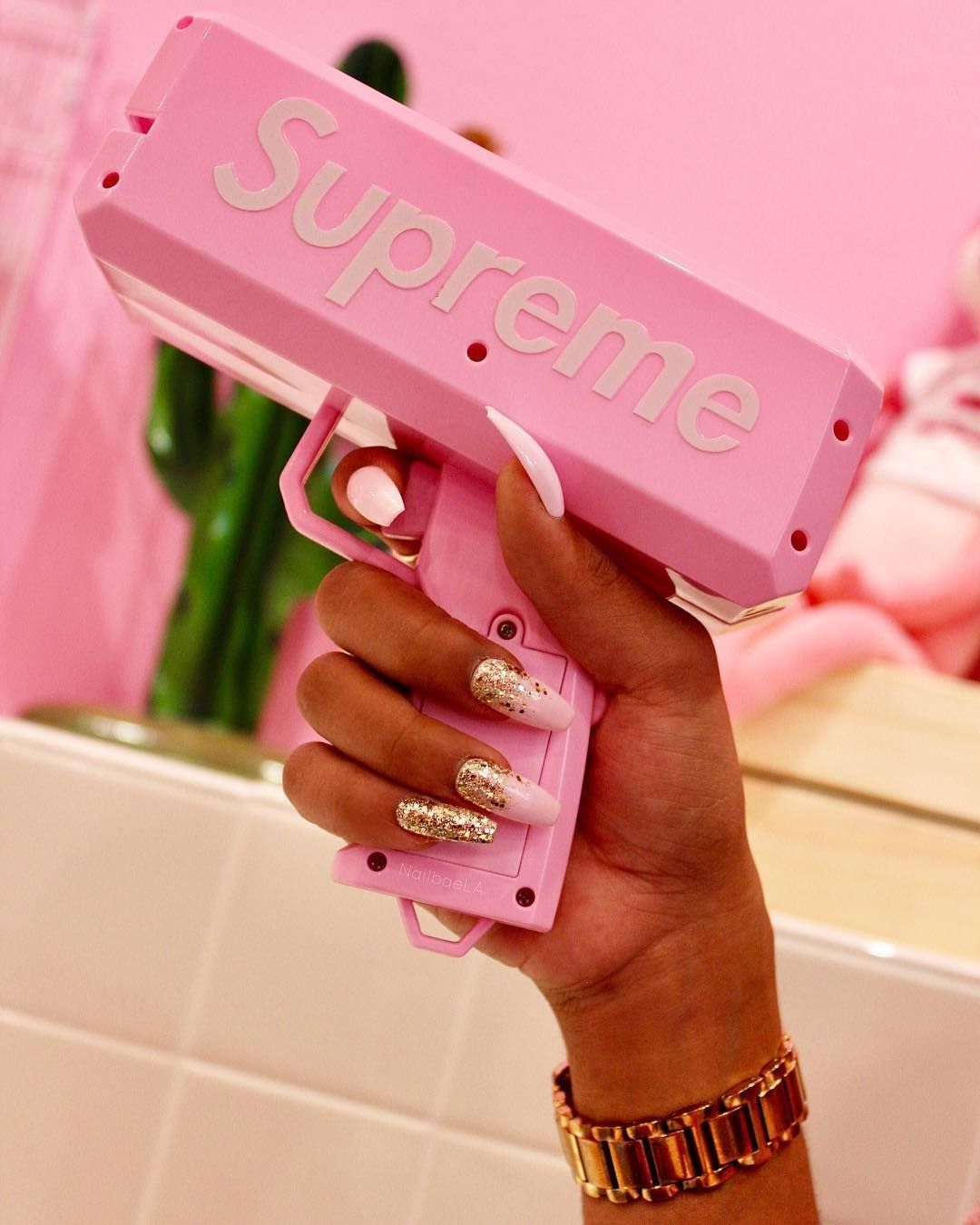 A hand with glittery nails holding a pink gun. - Nails, Supreme