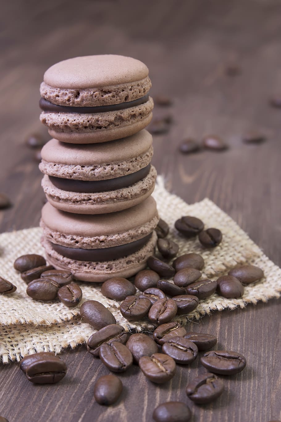 A stack of chocolate macarons with coffee beans on a wooden table - Chocolate, macarons