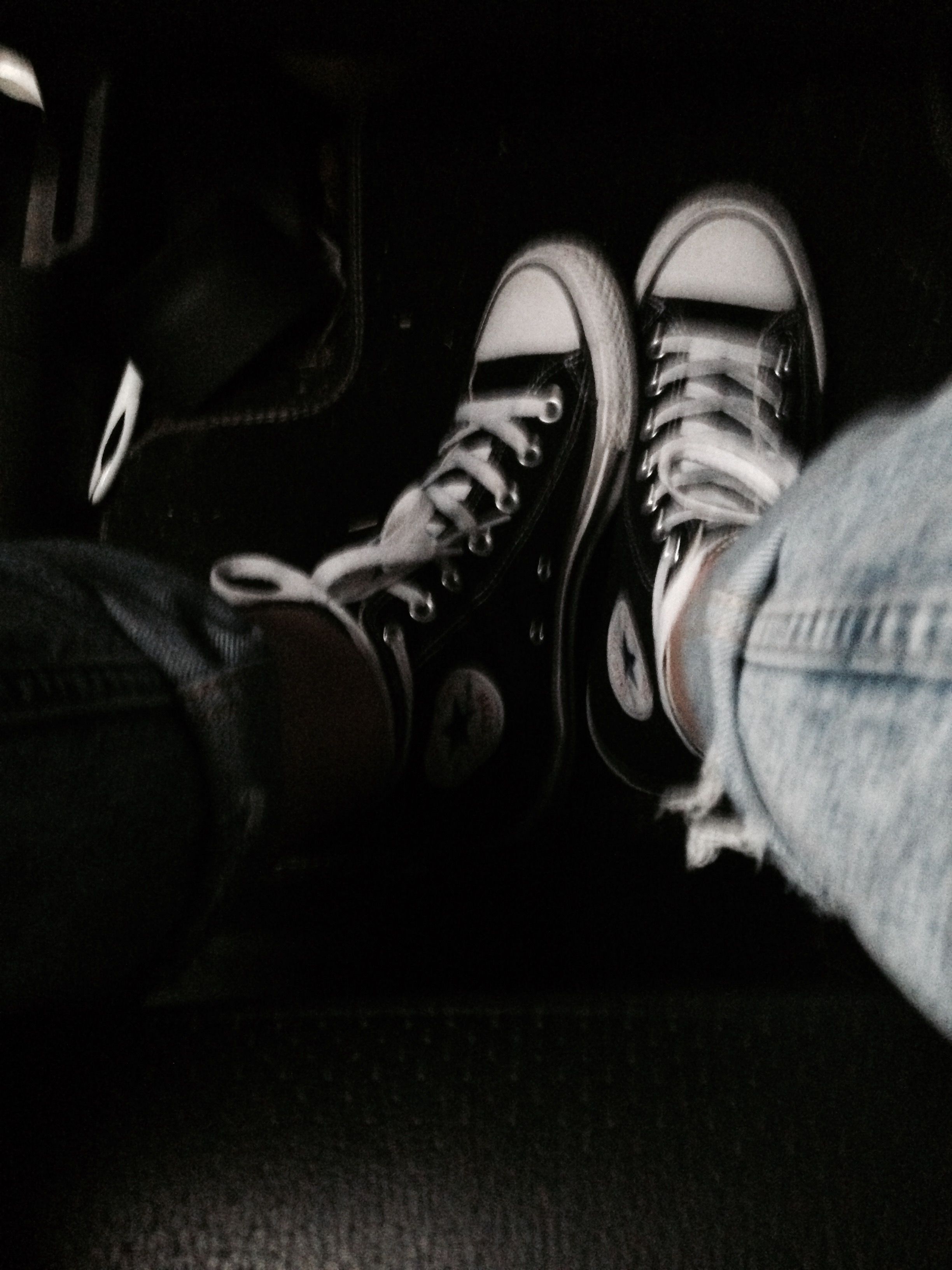 A pair of feet wearing converse sneakers are shown in a dark room. - Converse