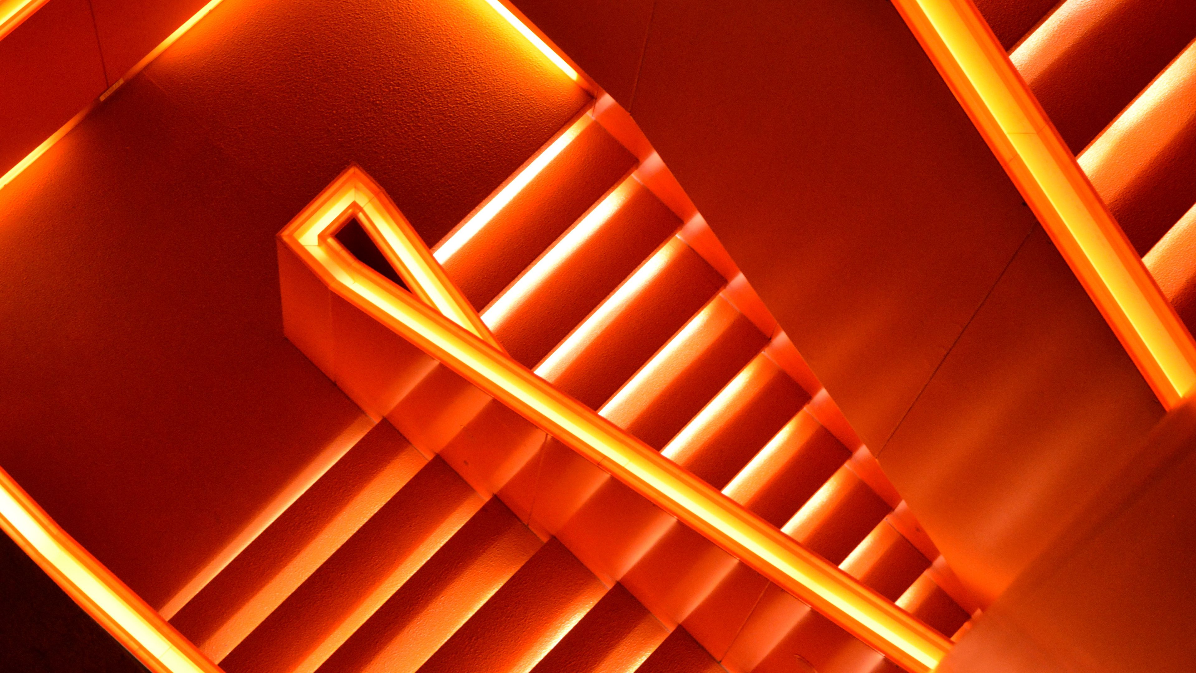 An orange neon light illuminates a flight of stairs. - Neon orange