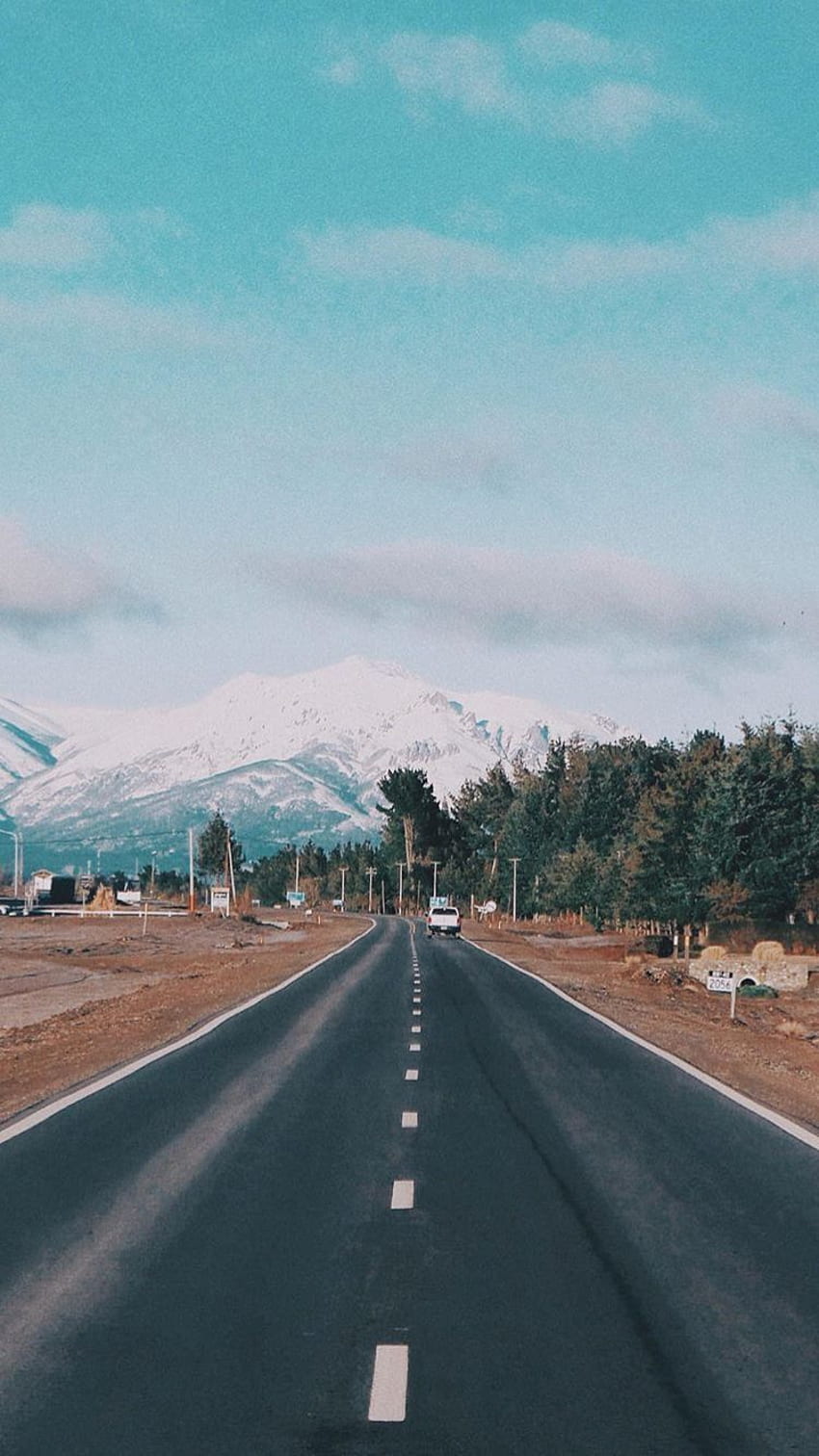 A road in the middle of a field with snow capped mountains in the background - Travel