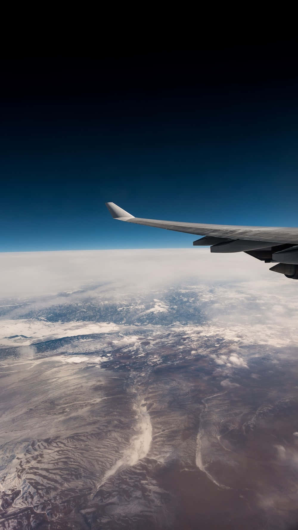 A plane wing is seen over a vast landscape of clouds and mountains. - Travel