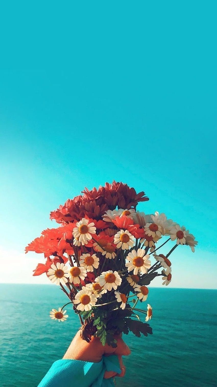 A person holding a bouquet of flowers in front of the ocean - Bright