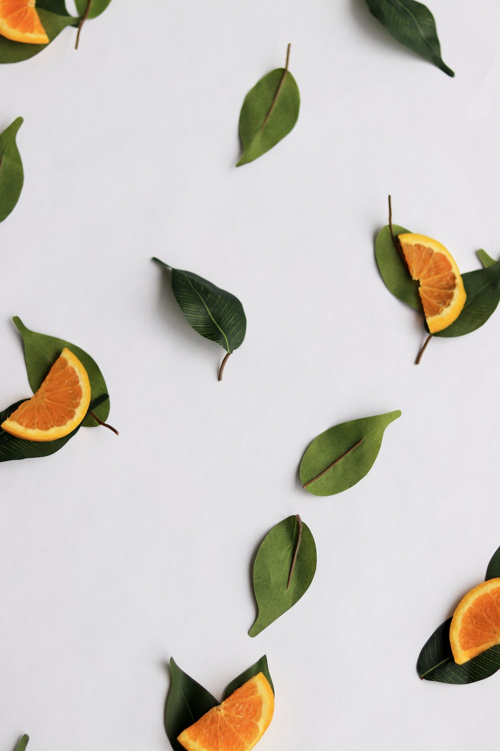 Orange slices and green leaves arranged on a white surface. - Fruit