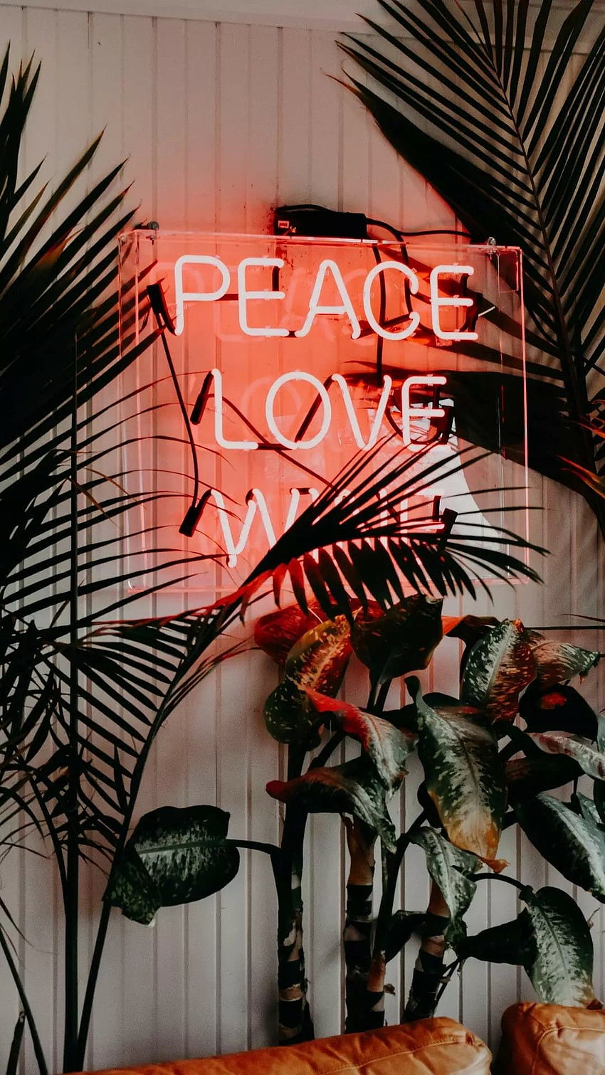 A neon sign that says peace love with plants surrounding it - Peace