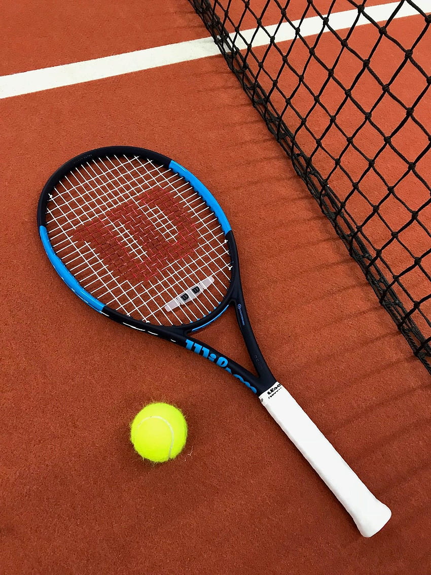 A tennis racket and ball on the ground next to the tennis net. - Tennis