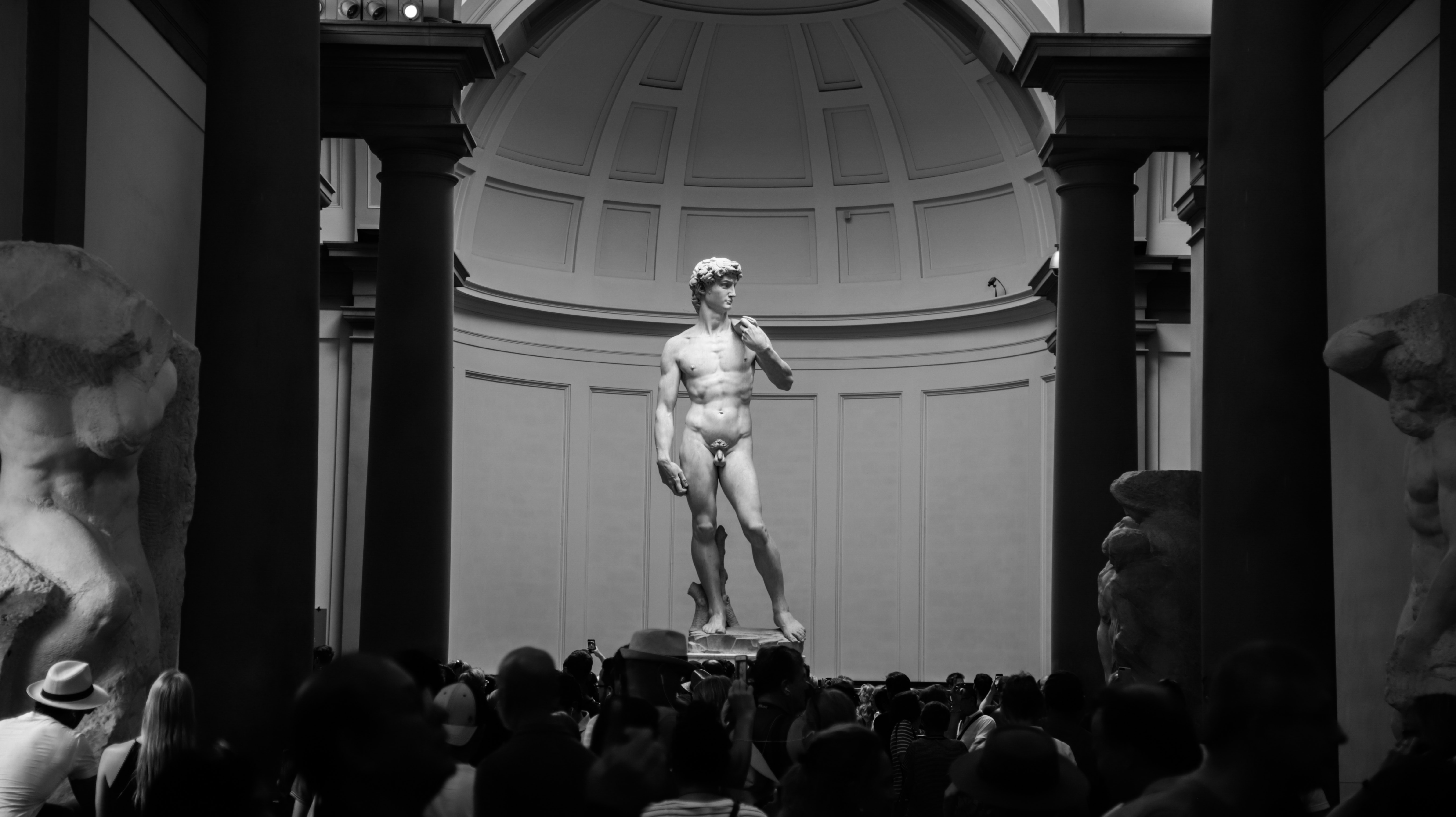 A black and white photo of people in front - Greek statue