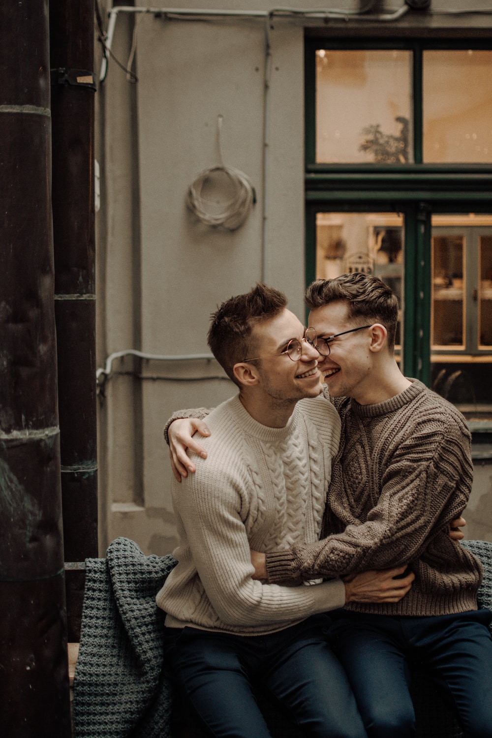 Two men in sweaters sit on a bench and smile at each other - Gay