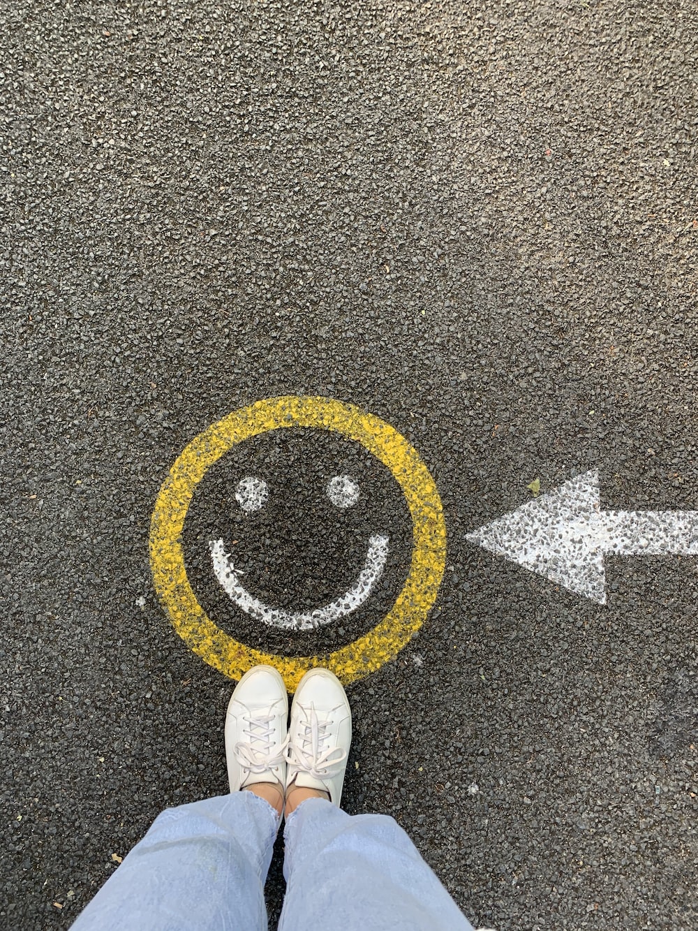 A person standing on the street with a smiley face drawn on the ground - Smile