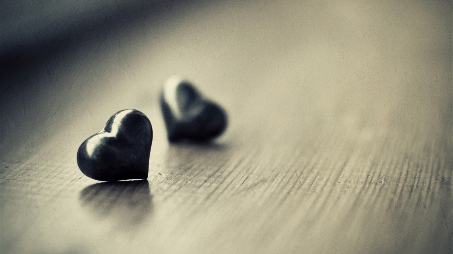 Two black hearts sitting on a wooden table - Black heart