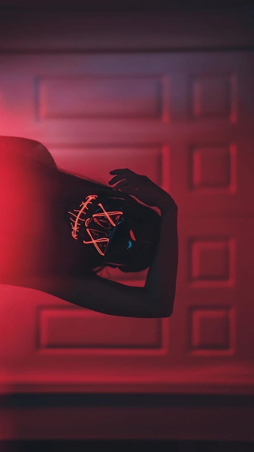 A person holding a neon mask in a red-lit room - Horror