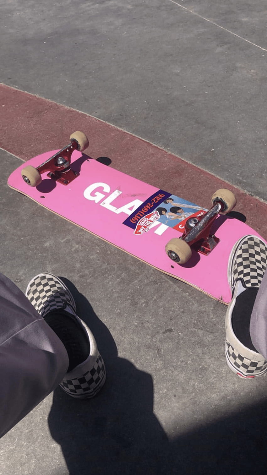 A person's feet in checkered shoes standing next to a pink skateboard. - Skate, skater