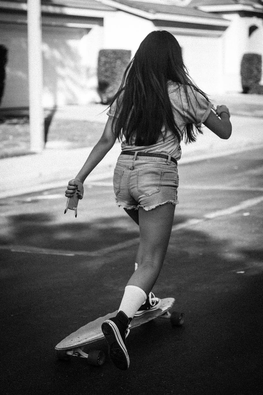 A girl with long hair rides a skateboard down a street. - Skate, skater