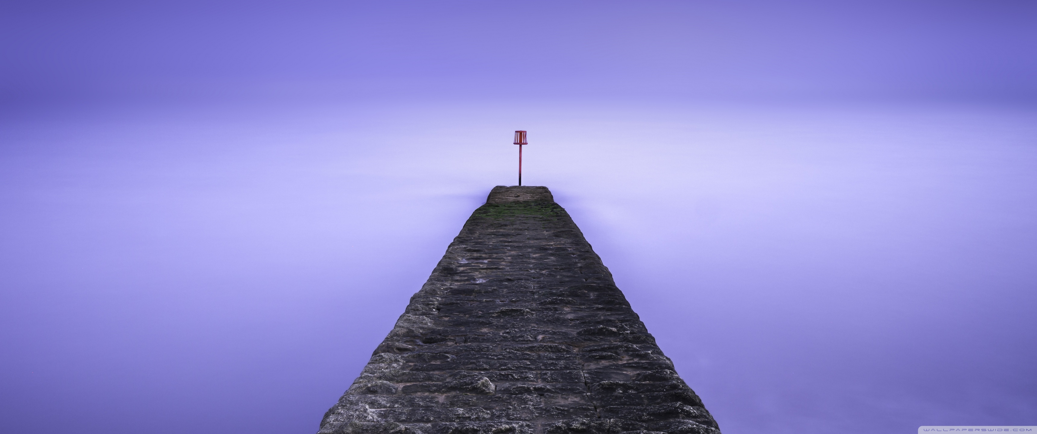 A stone pier leading to a red buoy on a purple background - 3440x1440
