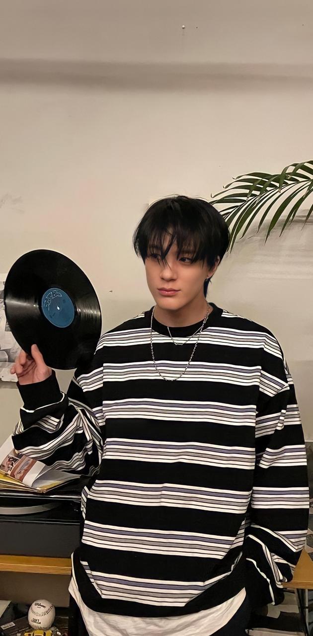 A person with black hair and a striped black and white shirt is holding a record. - NCT