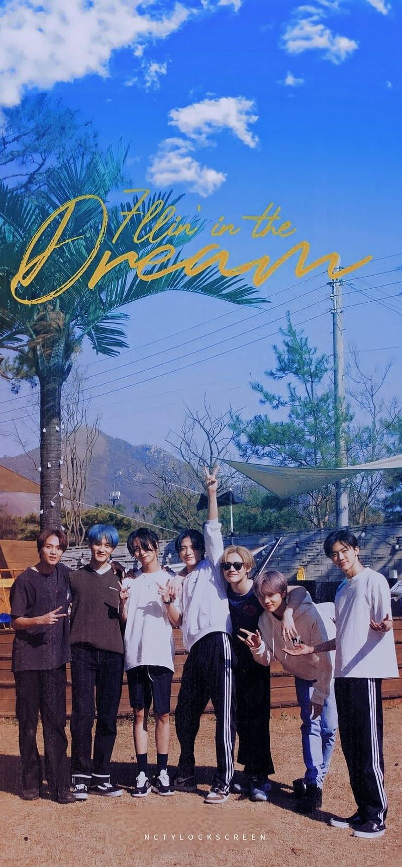 A beautiful group of NCT members on a tropical vacation, posing for a photo with palm trees in the background. The sky is blue and the sun is shining.  - NCT