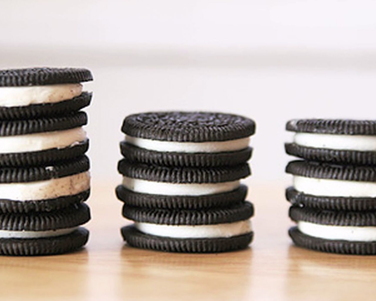 Three stacks of Oreo cookies, with the cookies sandwiching white cream, are stacked on a wooden table. - Oreo