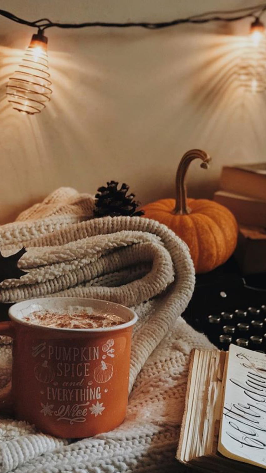 A cup of pumpkin spice latte sits on a blanket next to a book. - Fall, cozy, fall iPhone