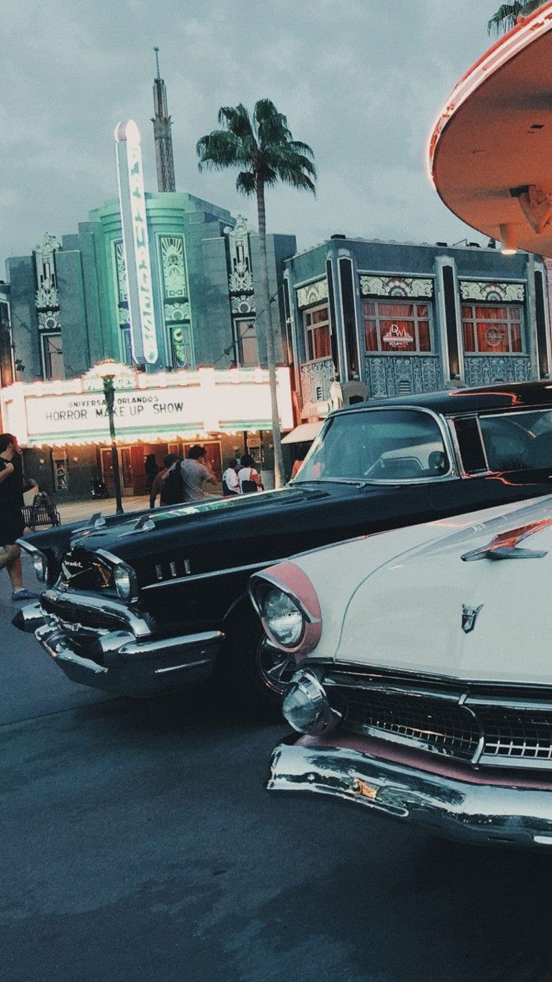 Classic cars are parked in front of a movie theater. - 50s