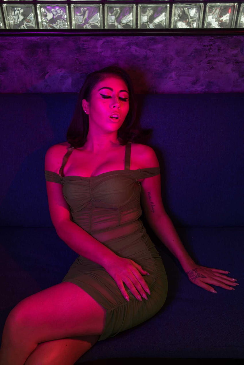 A woman in a dress sitting on a couch with a pink light on. - Kali Uchis