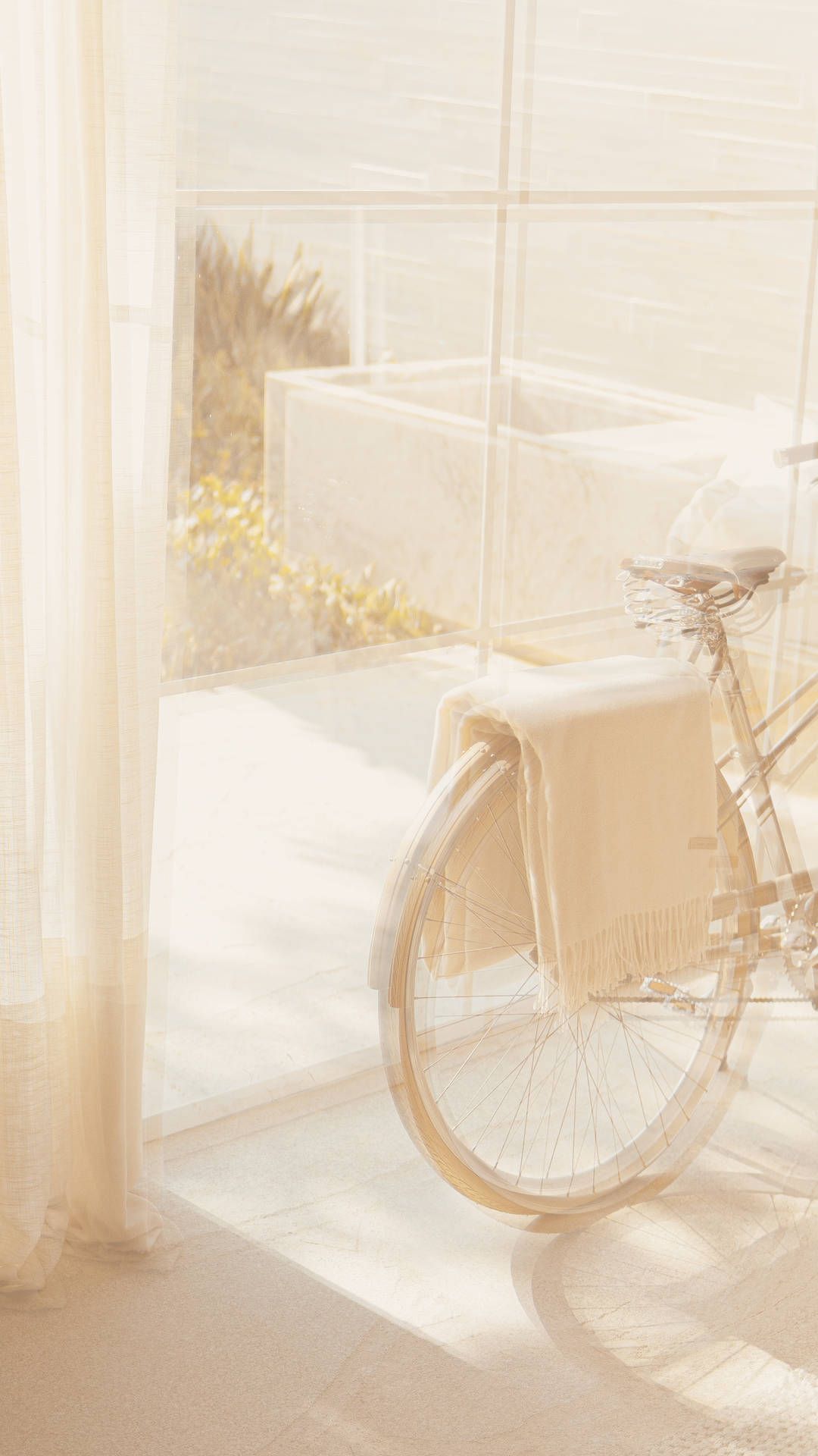 A white bicycle is parked next to a window with white curtains. - Cream